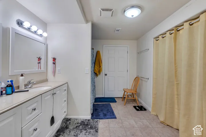 Bathroom featuring a white vanity cabinet with an integrated sink, a large wall-mounted mirror with a four-bulb vanity light, and tile flooring