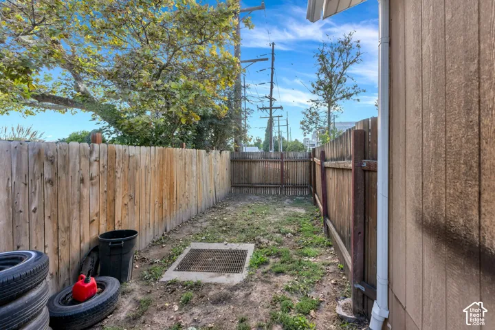 Enclosed side yard featuring wood fencing, a metal drainage grate, and exterior vertical siding