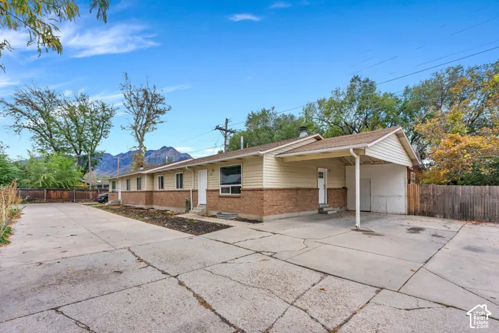 Single-level exterior featuring a brick and horizontal siding facade, expansive concrete driveway, covered carport, and mountain backdrop