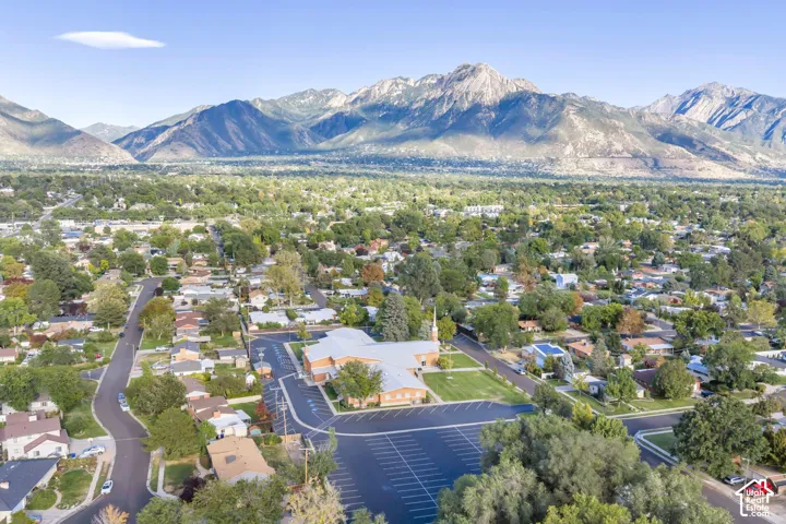 Aerial perspective featuring a large property with an expansive asphalt parking lot, manicured lawn areas, and a prominent mountain range backdrop