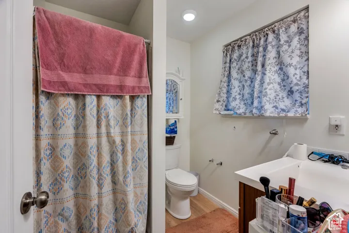 Bathroom featuring a single-sink vanity with an integrated countertop, wood-finish cabinetry, a white toilet, and a window with a recessed frame