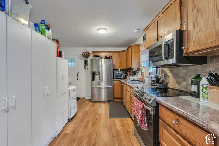 Kitchen featuring natural wood cabinetry, stainless steel appliances, stone-look countertops, a mosaic tile backsplash, and wood-finish flooring