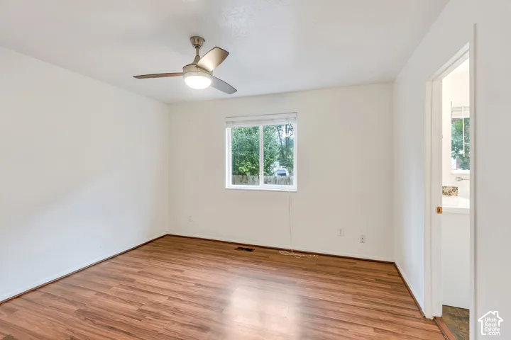 Interior room featuring wood-finish flooring, a neutral wall palette, a single-pane sliding window, and a ceiling-mounted light fixture with a fan