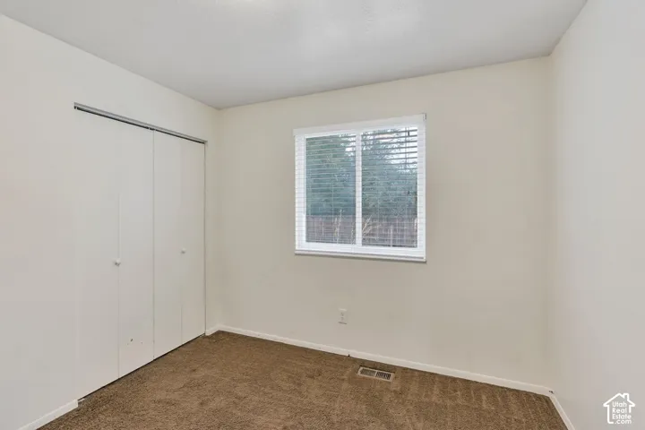 Interior room featuring neutral wall paint, carpeting, a single window with horizontal blinds, and a built-in closet with sliding doors