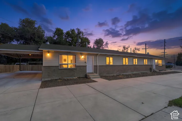Single-story exterior featuring a brick and horizontal siding facade, expansive concrete driveway, and attached carport