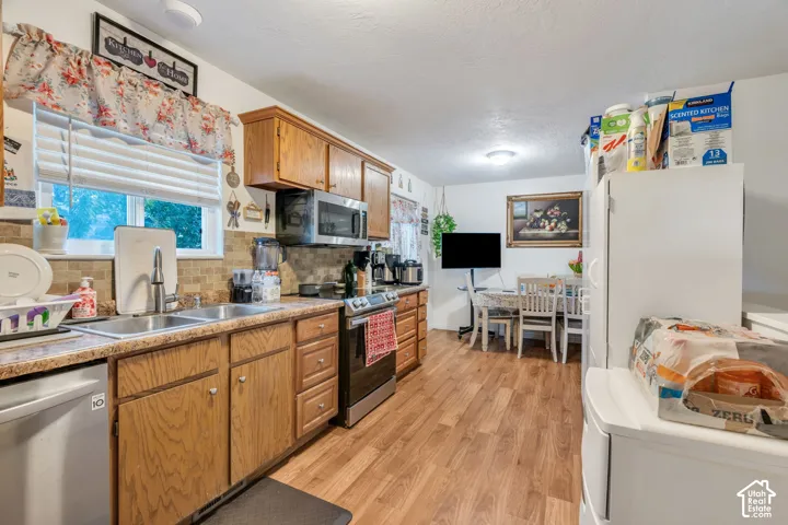 Kitchen featuring wood cabinetry, stainless steel appliances, dual-basin sink, stone-finish backsplash, and wood-finish flooring