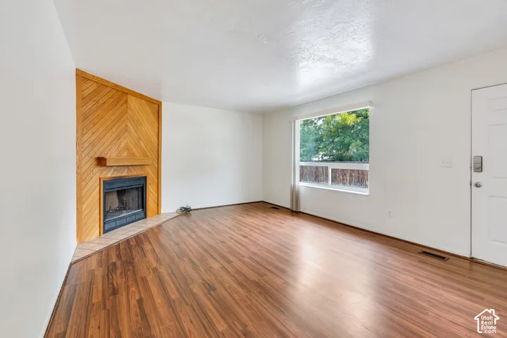 Wood-finish flooring, wood-paneled accent wall, fireplace with tile hearth, and large picture window