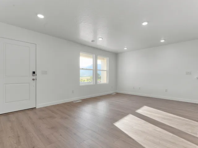 Bright, open living space featuring recessed ceiling lighting, gleaming wood-finish flooring throughout, and abundant natural light from dual windows