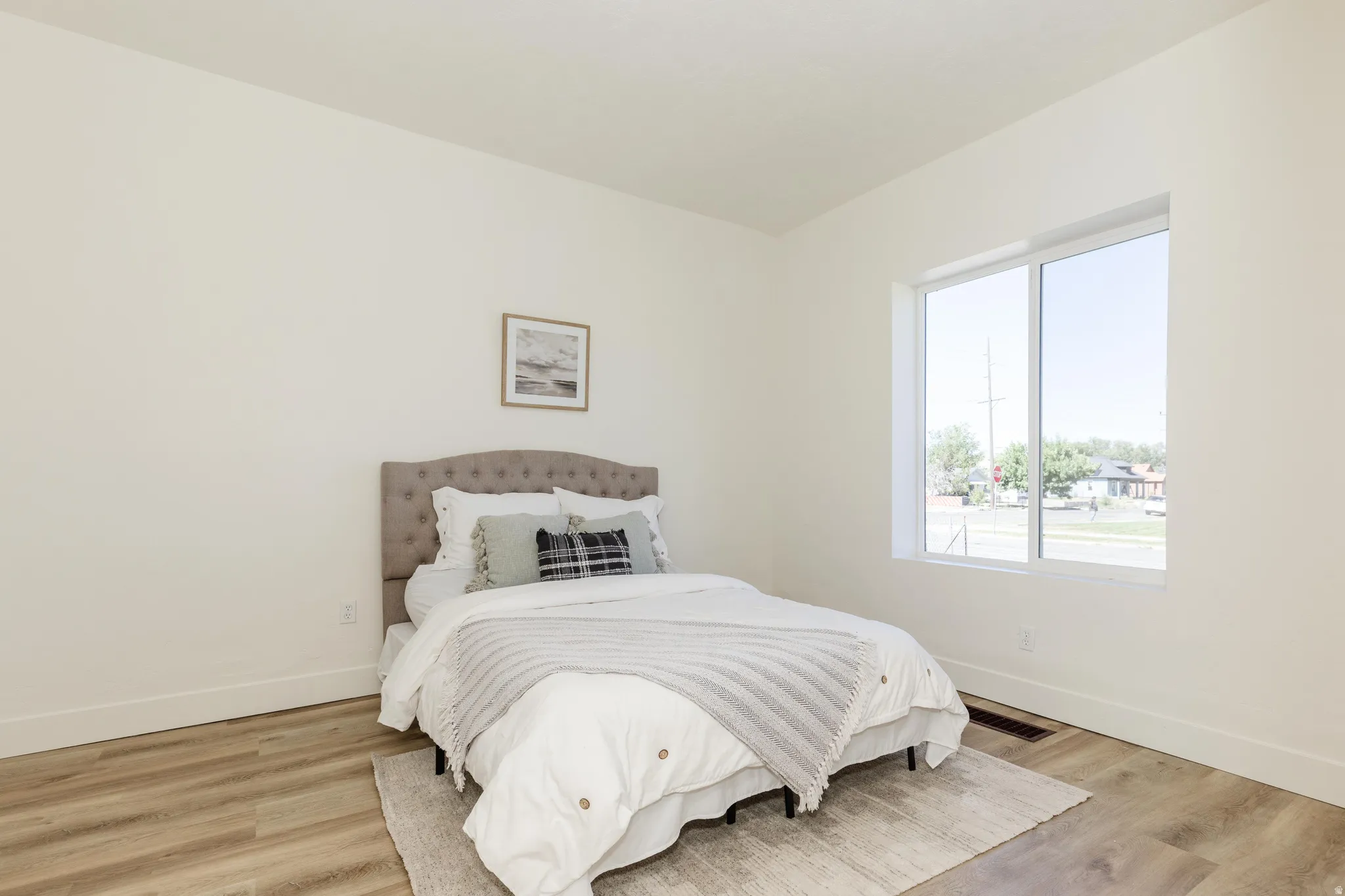 Light-filled room featuring a large window, neutral wall tones, wood-finish flooring, and white trim