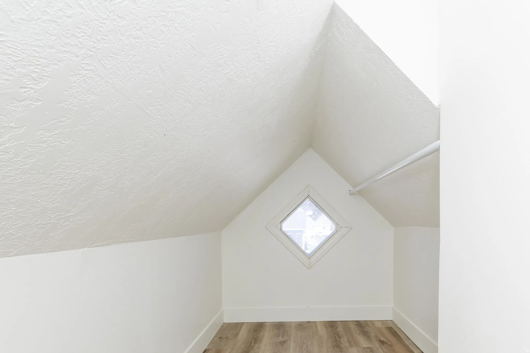 Attic space featuring wood-finish flooring, a diamond-shaped window, and a clothing rod