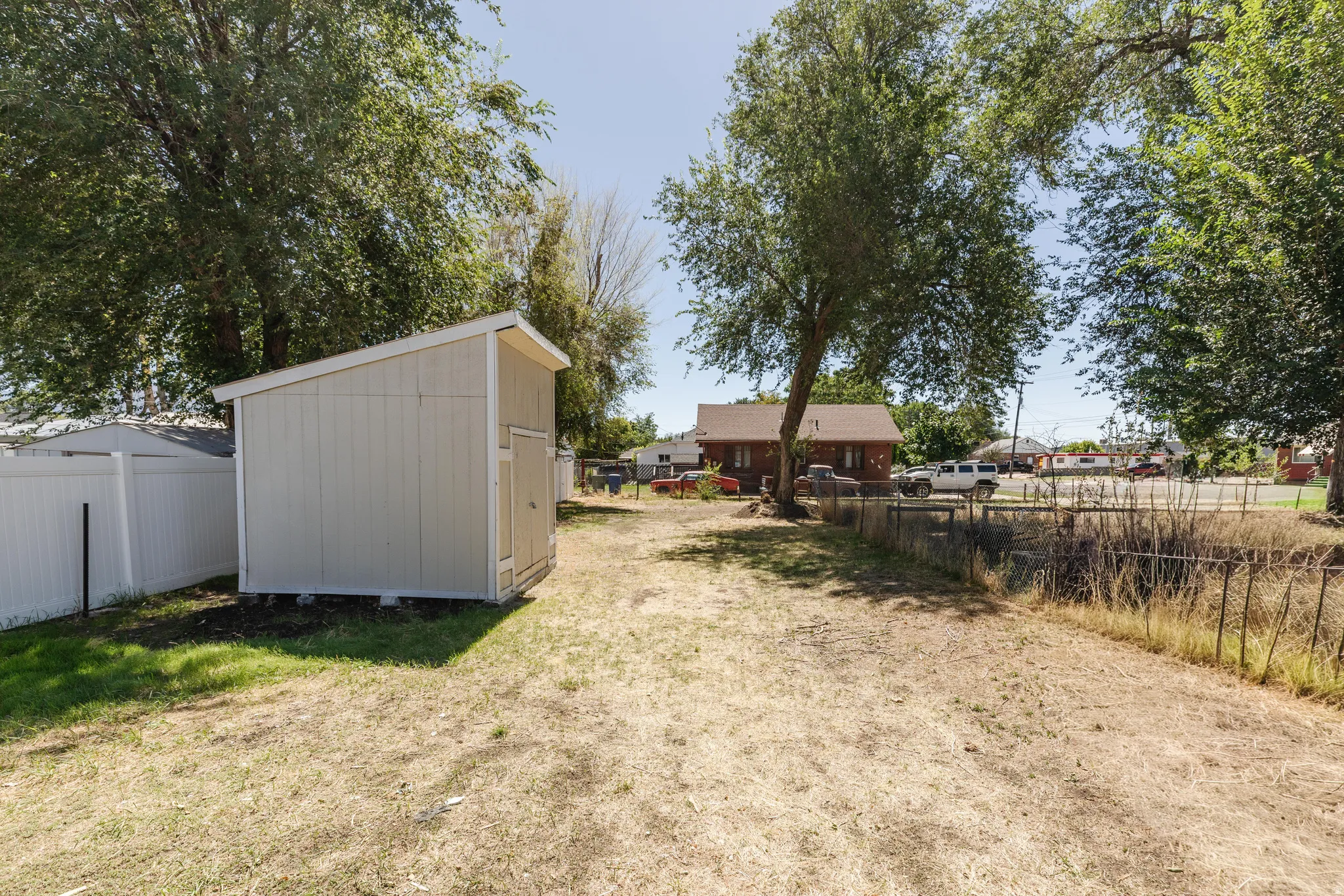 Backyard area featuring a storage shed, white privacy fence, and mature trees