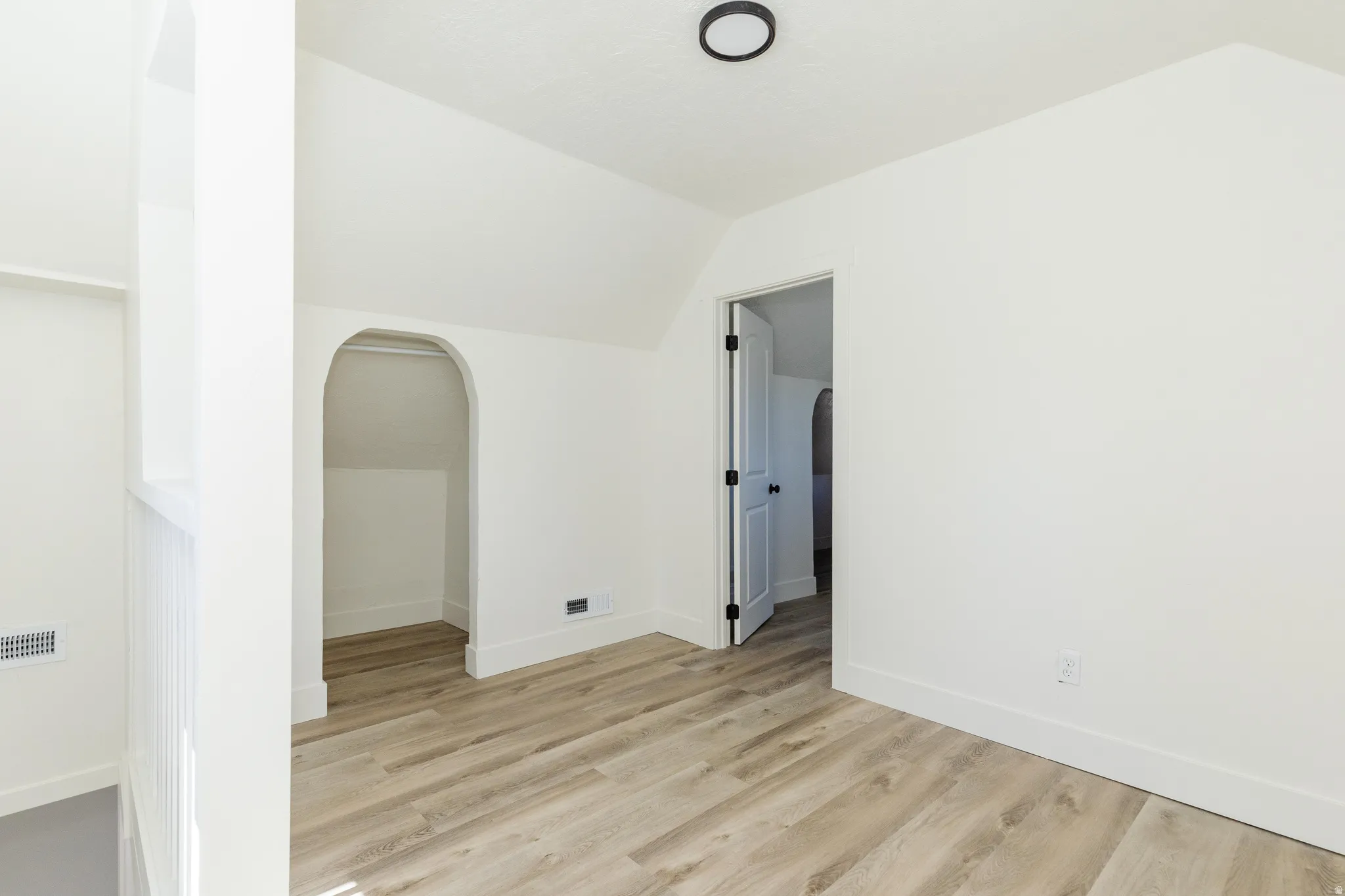 Wood-finish flooring, white walls, arched alcove, and a modern flush-mount ceiling light