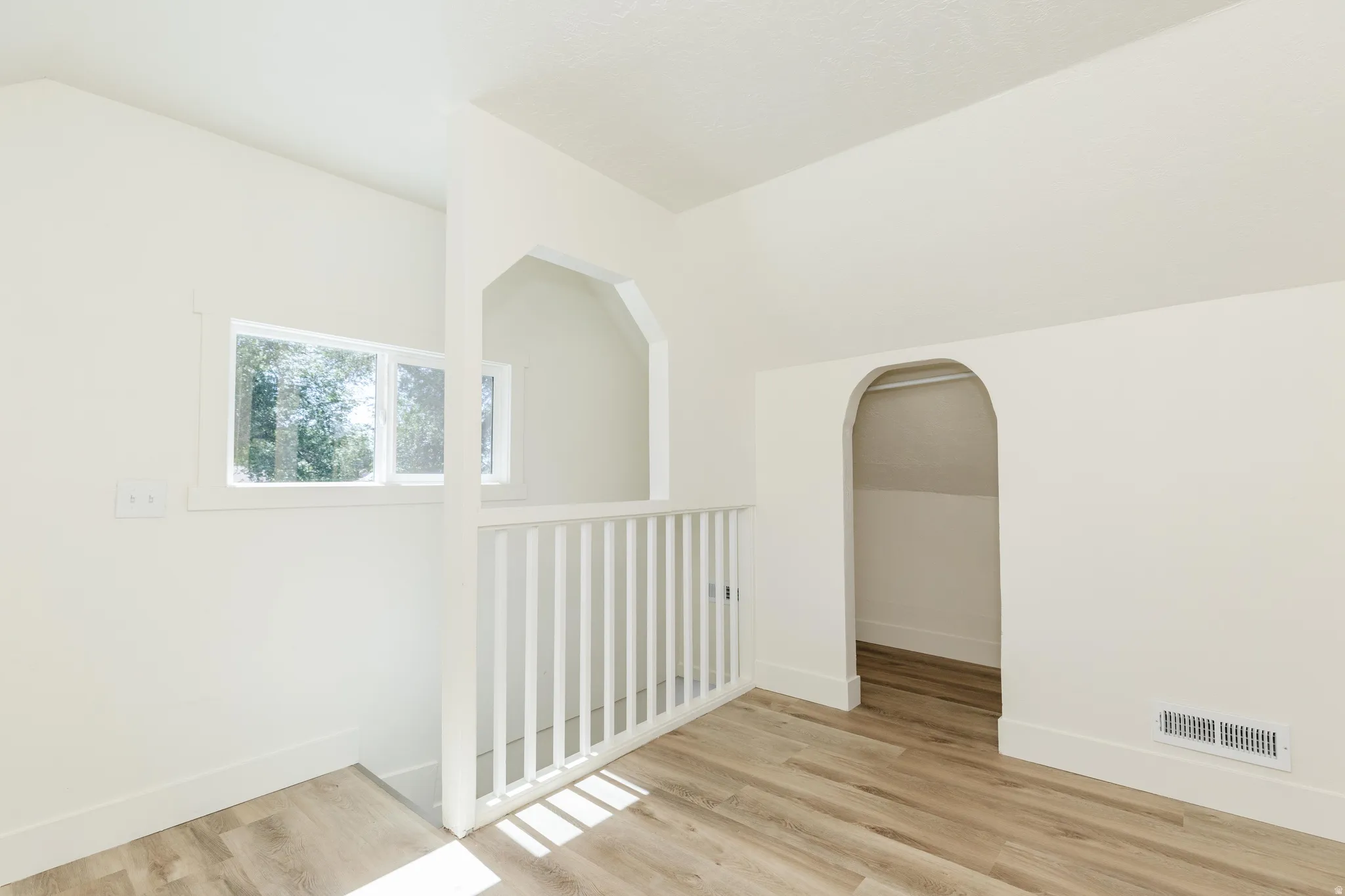 Sloped ceilings, arched doorways, white painted railing, wood-finish flooring, and white walls