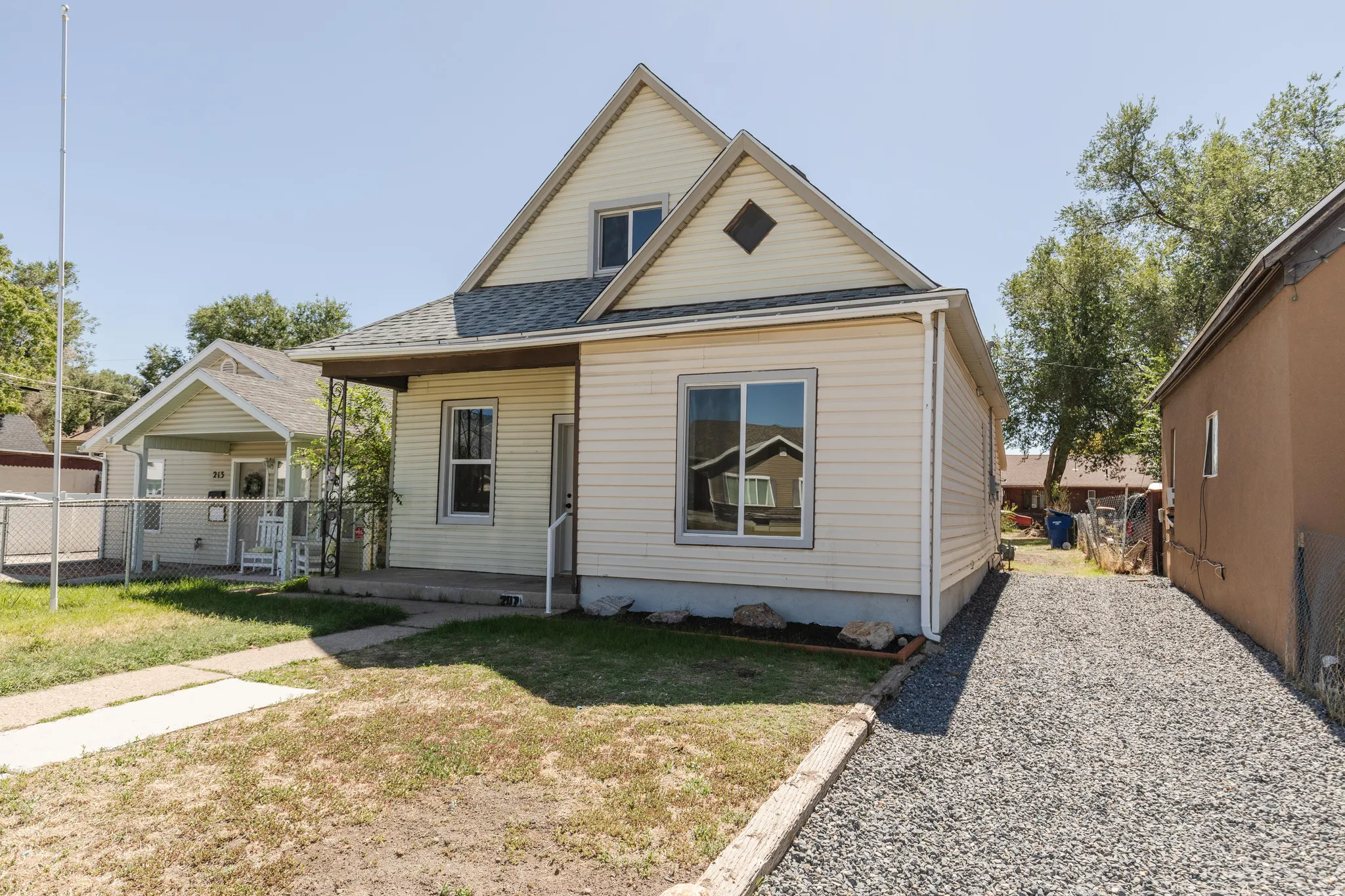 Gabled roofline, siding exterior, covered porch, gravel driveway, and a front yard