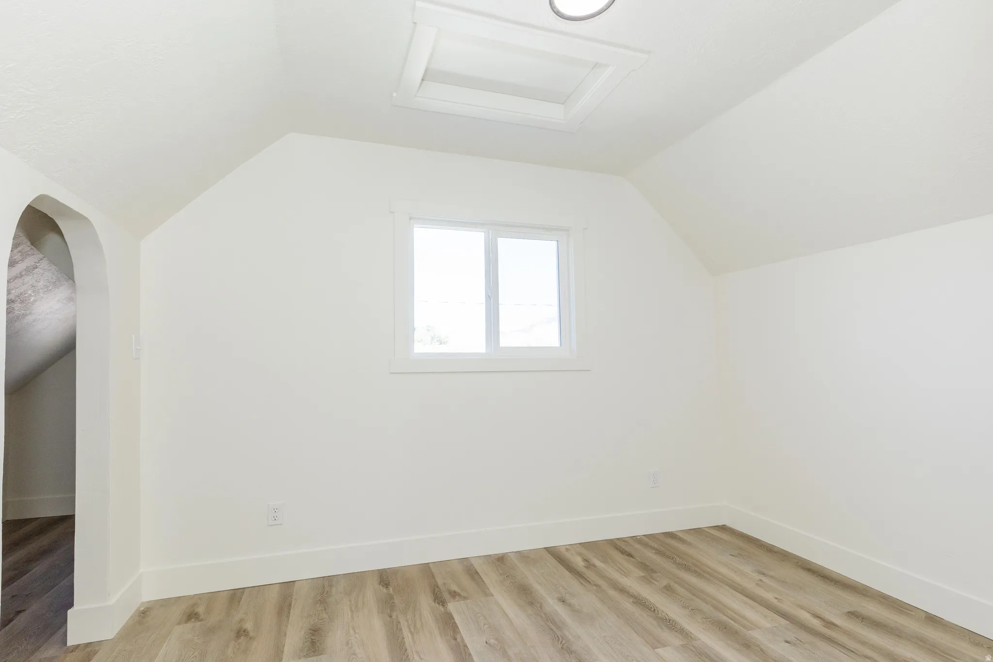 Wood-finish flooring, white walls, window, recessed lighting, and an arched entry