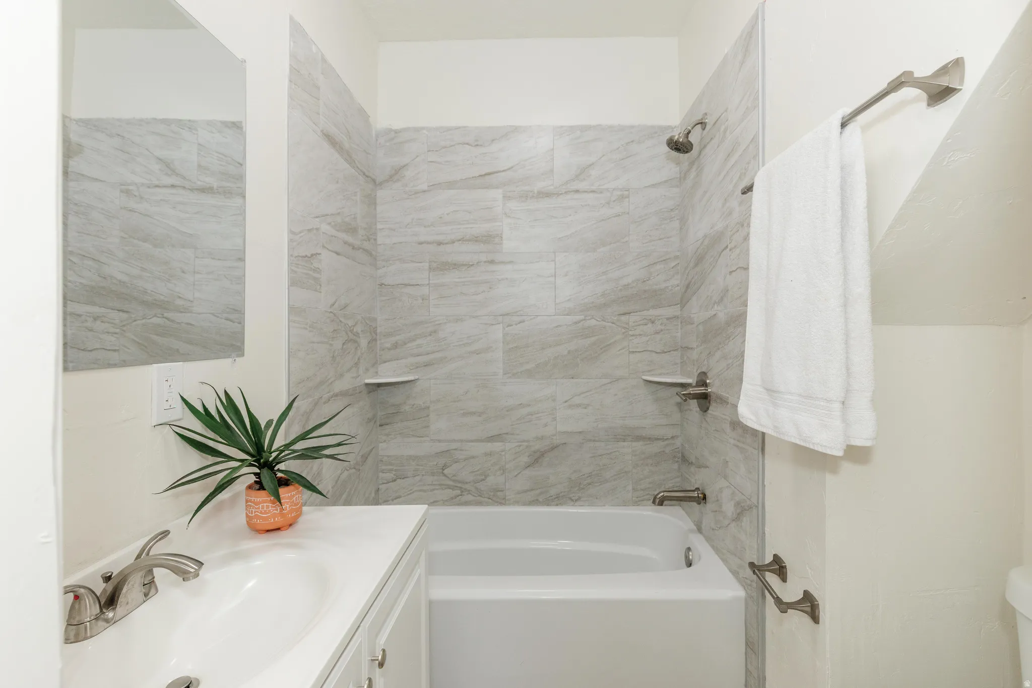 Full-size bathtub with tiled surround, shower fixture, and vanity with integrated sink and brushed nickel faucet