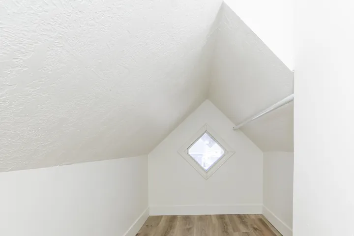 Attic space featuring wood-finish flooring, a diamond-shaped window, and a clothing rod