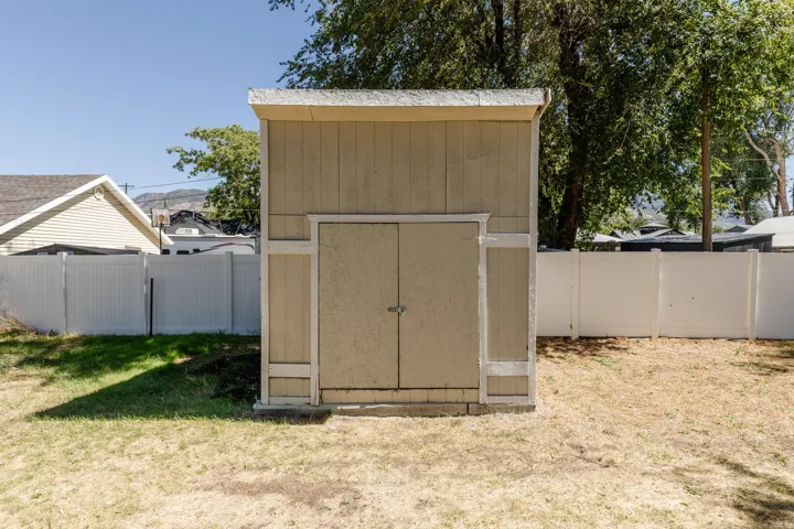 Detached storage shed with double doors, wood siding, and a white vinyl fence