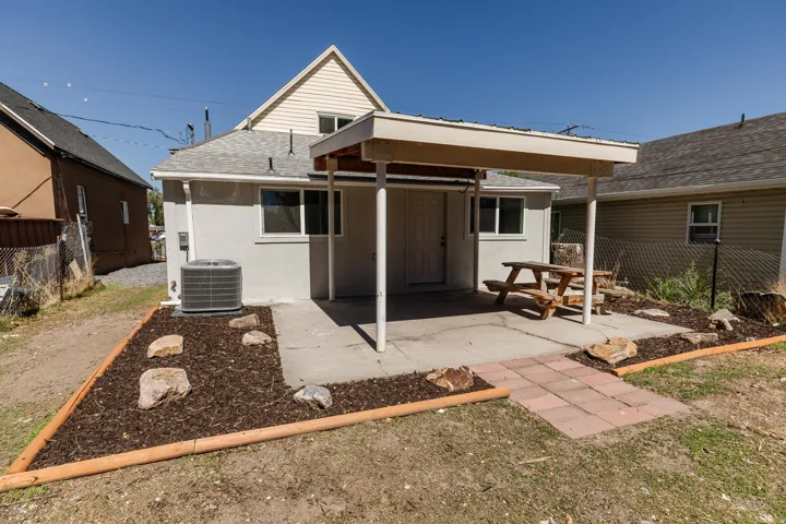 Rear patio with a covered section, concrete surface, and landscape beds