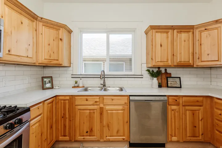 Kitchen featuring light wood cabinetry, a subway tile backsplash, light-toned countertops, a stainless steel dishwasher, and a double basin sink with a gooseneck faucet