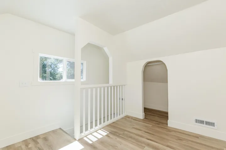 Sloped ceilings, arched doorways, white painted railing, wood-finish flooring, and white walls