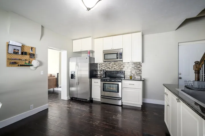 Kitchen featuring wood-finish flooring, white cabinetry, stainless steel appliances, and a tiled backsplash
