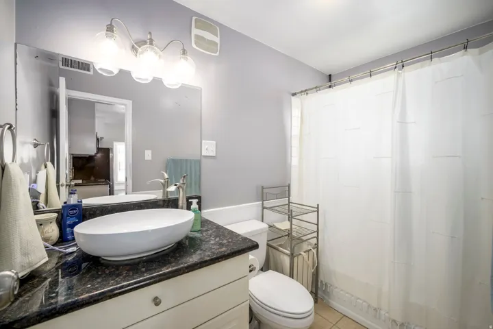 Vanity with a vessel sink, dark granite countertop, and light-toned cabinetry