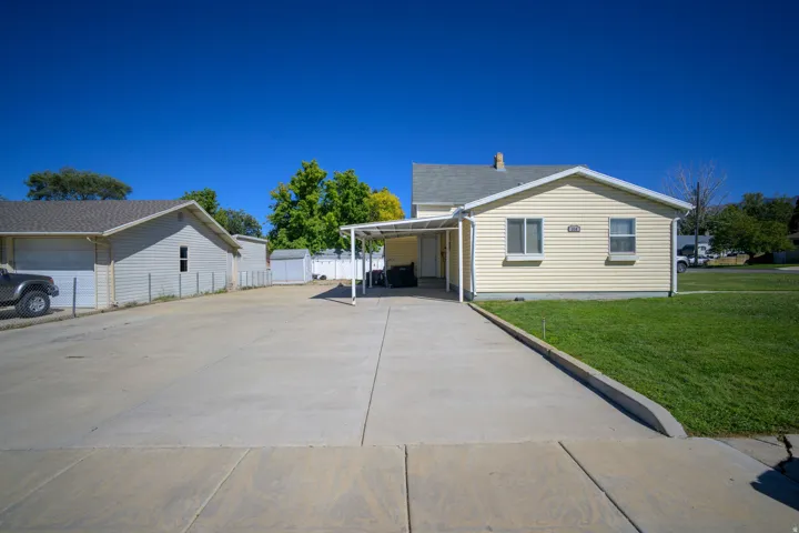 Concrete driveway leading to a covered carport, expansive concrete parking area, detached two-car garage, and a separate storage shed