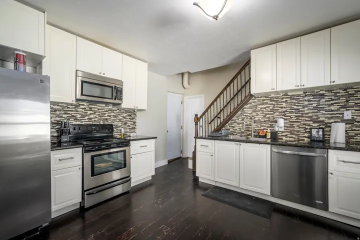 Kitchen featuring white cabinetry, dark stone countertops, stainless steel appliances, and a mosaic tile backsplash