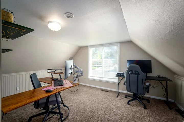 Carpeted room featuring a window with blinds, sloped ceiling, and beadboard wainscoting