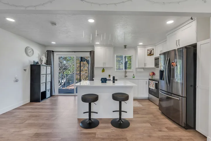 Open-concept kitchen featuring an island with a breakfast bar, white cabinetry, stainless steel appliances, and wood-finish flooring