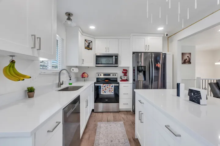 White cabinetry, stainless steel appliances, wood-finish flooring, white countertops, and an integrated kitchen island