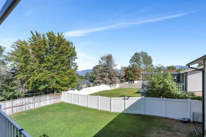 Expansive backyard featuring a green lawn, mature trees, and a white privacy fence