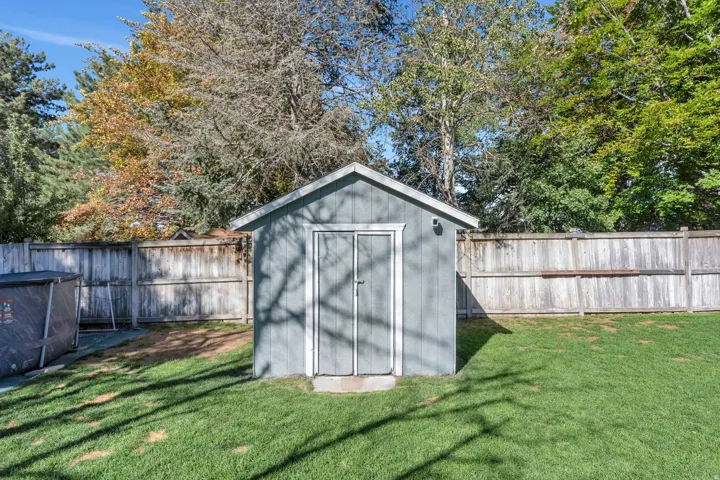 Manicured lawn with a storage shed featuring double doors and a wood fence