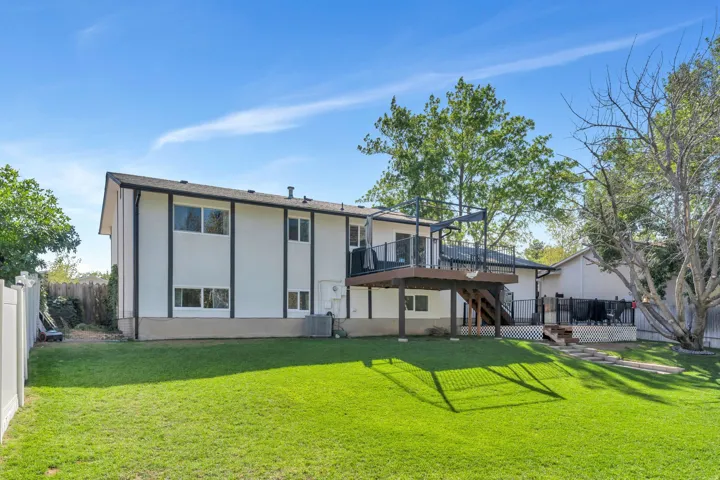 Expansive green lawn, multi-level wood deck with black railings, white privacy fencing, and mature trees