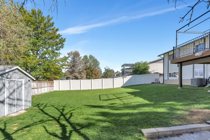 Expansive grassy yard with a storage shed, white privacy fencing, and a raised exterior deck with metal railings