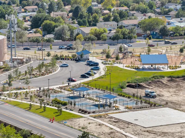 Expansive park area featuring tennis courts, covered seating, playground equipment, and a large grass lawn