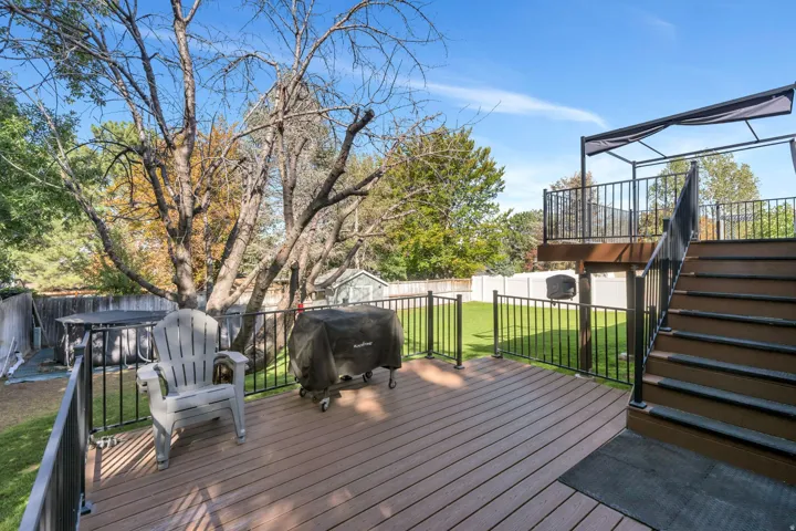 Composite deck with black metal railings, leading to a tiered deck with a canopy structure, and a fenced yard with artificial turf