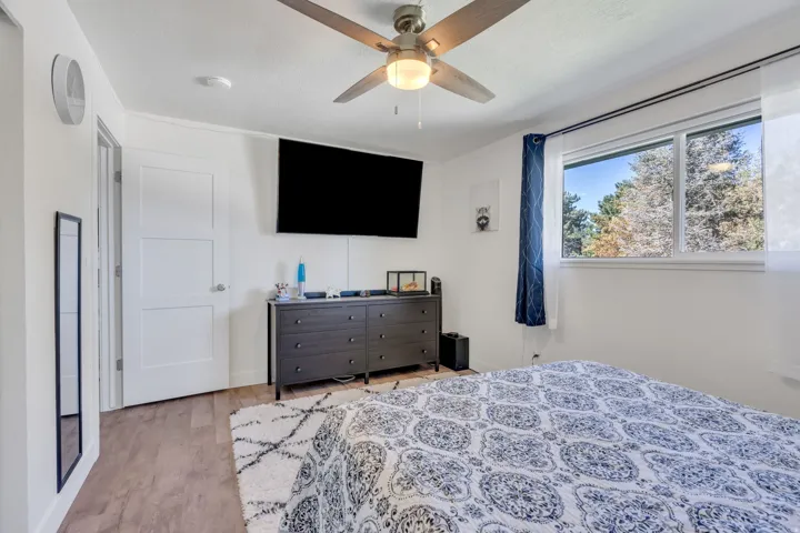 Wood-finish flooring, white paneled door, ceiling fan with integrated lighting, and a large window