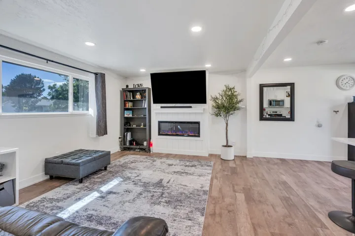 Recessed lighting, wood-finish flooring, white walls, and a built-in fireplace with a mantel