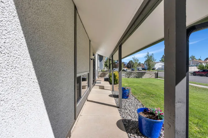 Covered front porch with concrete walkway, stucco exterior, and manicured lawn