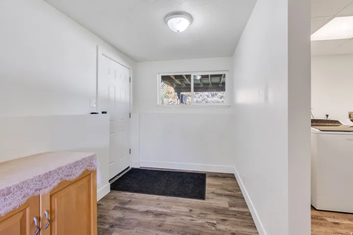 White paneled entry door, wood-finish flooring, white walls with wainscoting, and a flush mount ceiling light