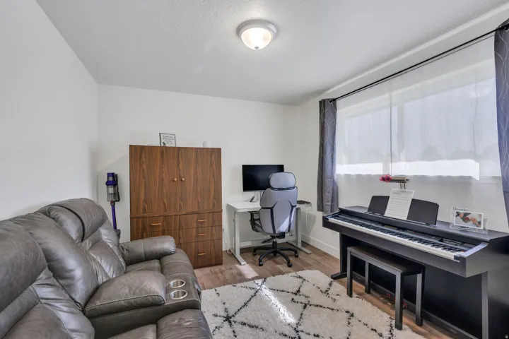 Wood-finish flooring, white walls, and a window with roller shades and drapery