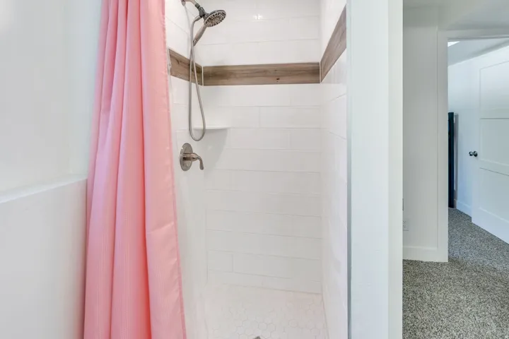 White subway tile shower surround with a wood-finish accent band, hexagonal floor tiles, and a built-in shower niche