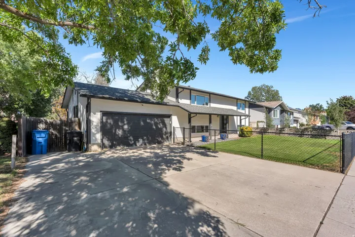 Two-story stucco exterior with a covered porch, attached two-car garage, and a chain-link fence enclosing a manicured lawn