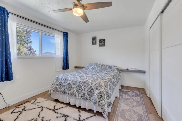 Wood-finish flooring, white walls, double window with mountain scenery, ceiling fan with integrated lighting, and white sliding closet doors