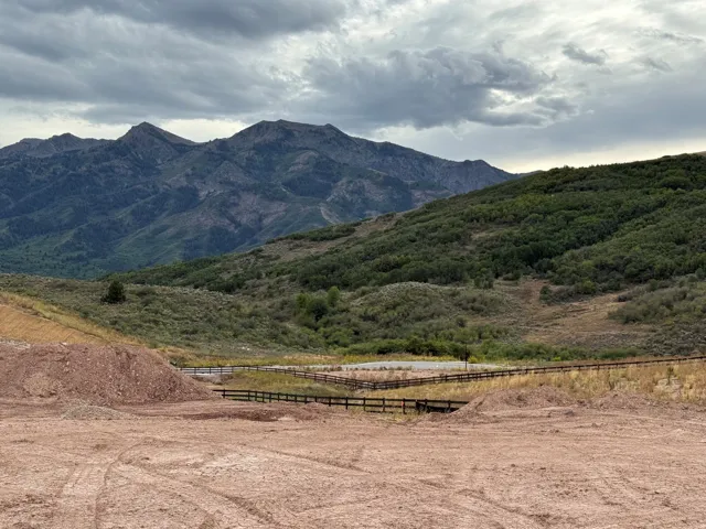Expansive lot featuring a dirt surface, a dark wooden fence, and distant mountainous terrain