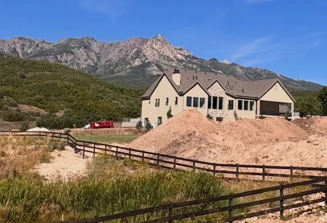 Mountain backdrop, two-story residence, multiple windows, covered patio space, and wood fence