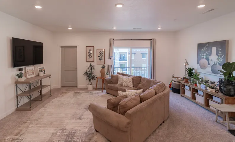 Recessed lighting, light gray painted walls, a built-in wall-mounted television, a neutral-toned door, and a sliding glass door with balcony access