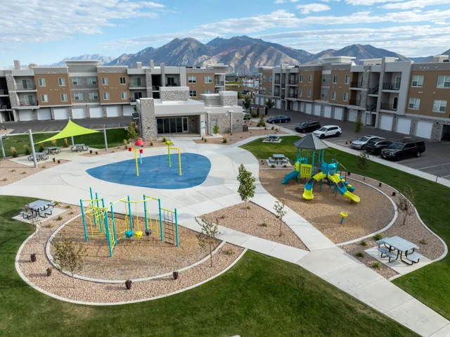Community green space featuring multiple playgrounds, picnic areas, a splash pad, and mountain backdrop